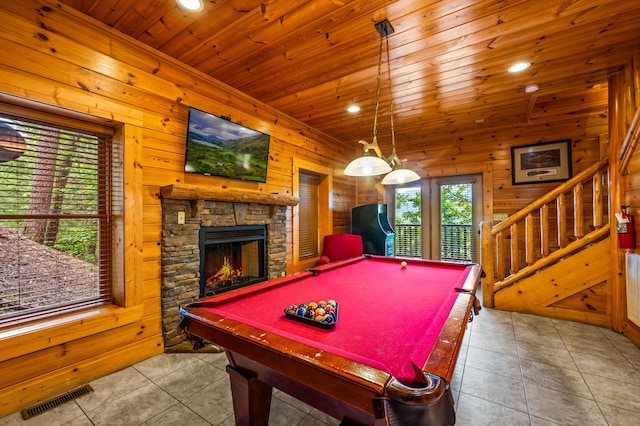 recreation room with a stone fireplace, light tile patterned floors, wooden ceiling, and wooden walls