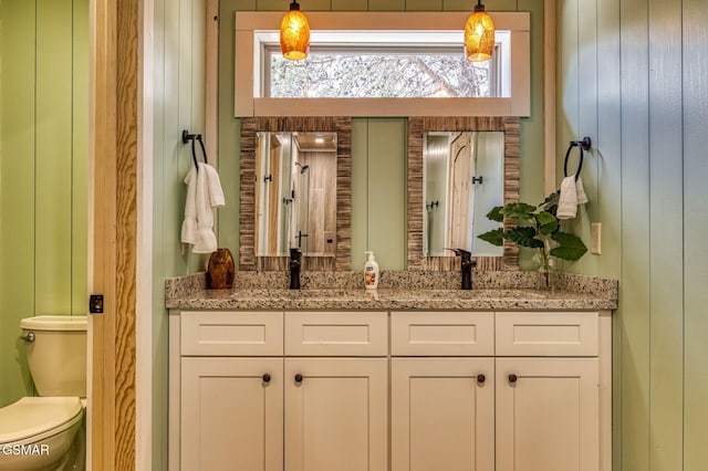 bathroom featuring double vanity, toilet, and wood walls