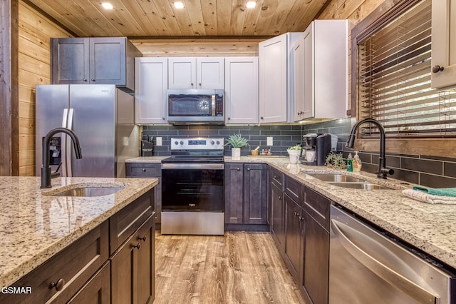 kitchen featuring appliances with stainless steel finishes, a sink, wooden ceiling, light wood-type flooring, and tasteful backsplash