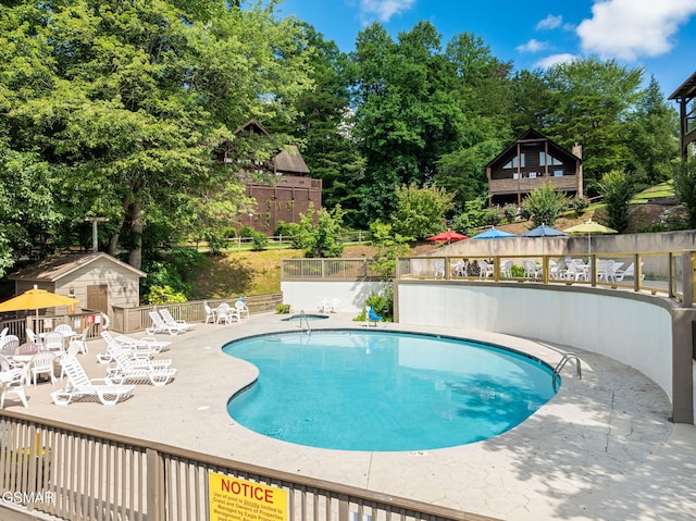 community pool with fence, a patio, and view of scattered trees