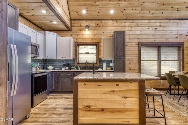 kitchen featuring appliances with stainless steel finishes, light wood-style flooring, a center island with sink, light stone counters, and a kitchen breakfast bar