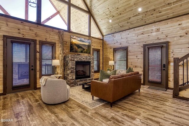 living area with high vaulted ceiling, wood walls, wood finished floors, a stone fireplace, and stairs