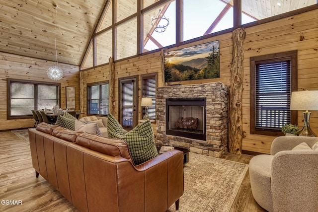 living room featuring wood walls, high vaulted ceiling, light wood-style flooring, a fireplace, and plenty of natural light