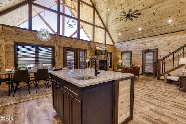 kitchen with a sink, high vaulted ceiling, dark brown cabinetry, a stone fireplace, and light wood-style flooring
