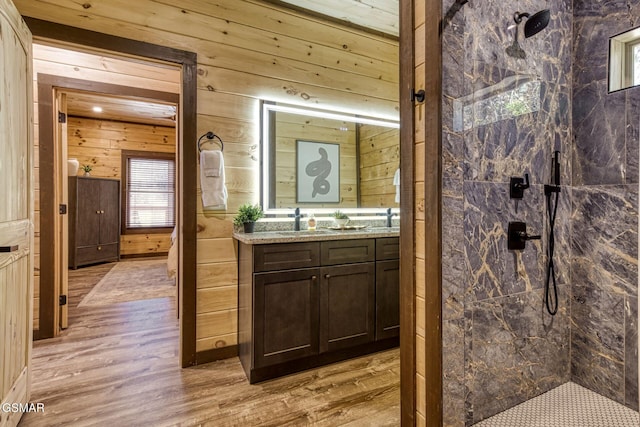 full bathroom featuring wood walls, wood finished floors, a marble finish shower, and vanity