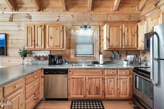 kitchen with sink, wooden walls, stainless steel appliances, and light hardwood / wood-style floors