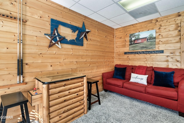 living room featuring a paneled ceiling, wooden walls, and carpet floors