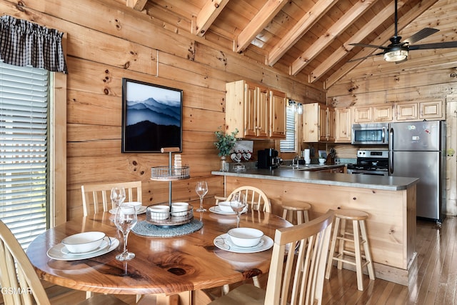 dining room with dark hardwood / wood-style floors, wooden walls, vaulted ceiling with beams, ceiling fan, and wood ceiling