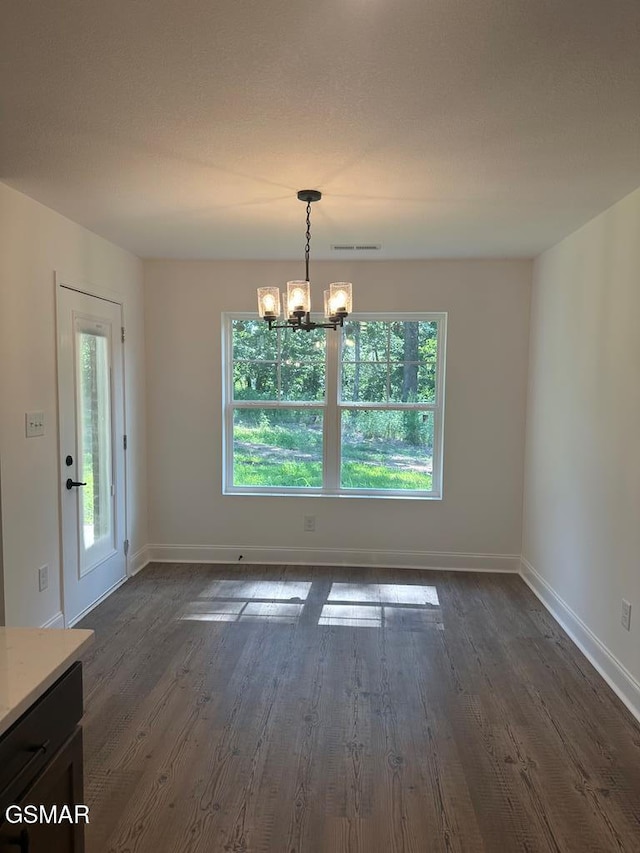 unfurnished dining area with baseboards, dark wood finished floors, a notable chandelier, and visible vents