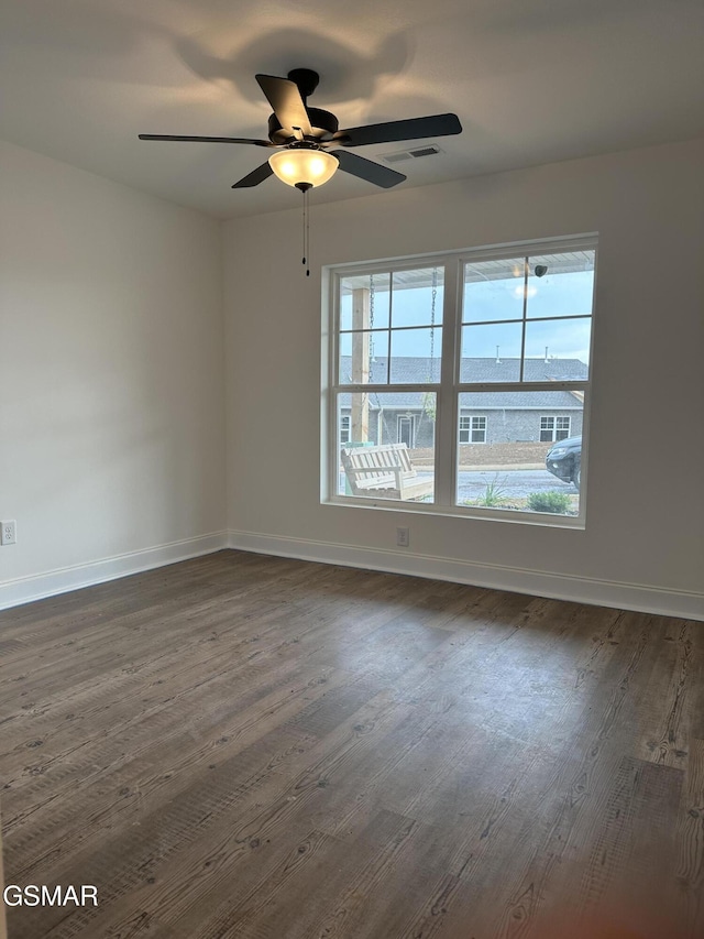 unfurnished room featuring baseboards, ceiling fan, dark wood finished floors, and visible vents