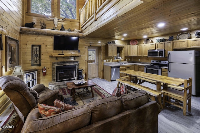 living room with sink, a stone fireplace, light hardwood / wood-style flooring, a towering ceiling, and wood ceiling