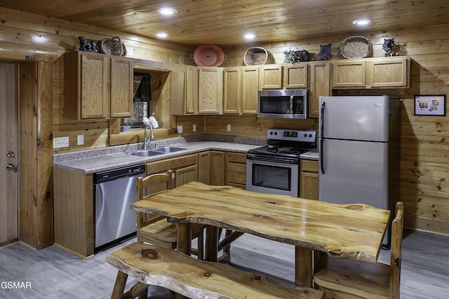 kitchen featuring appliances with stainless steel finishes, light brown cabinetry, wooden walls, sink, and light hardwood / wood-style flooring