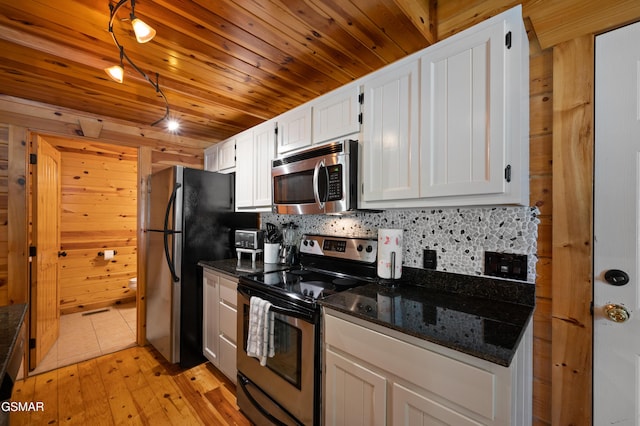 kitchen featuring wooden walls, dark stone countertops, decorative backsplash, white cabinets, and appliances with stainless steel finishes