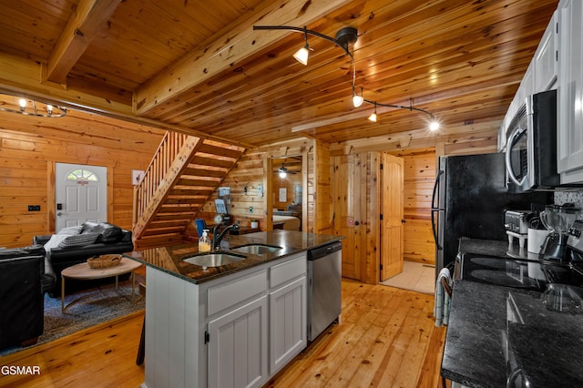 kitchen featuring sink, stainless steel appliances, wood walls, a kitchen island with sink, and white cabinets