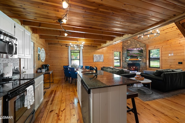 kitchen with white cabinets, light hardwood / wood-style flooring, appliances with stainless steel finishes, beam ceiling, and a breakfast bar area