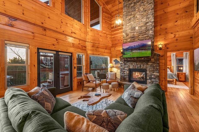 living room with wood walls, wood-type flooring, french doors, and a stone fireplace