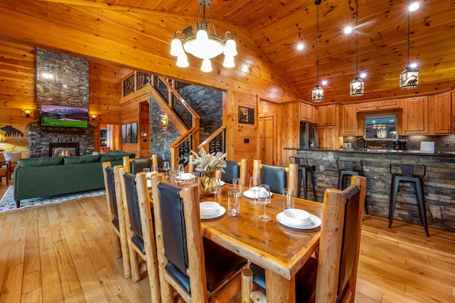 dining space with high vaulted ceiling, a stone fireplace, light wood-style flooring, and wooden walls