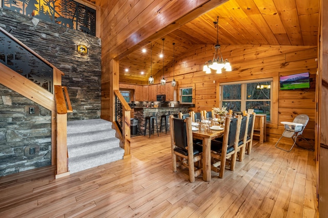 dining area with light wood-style flooring, stairway, an inviting chandelier, wood ceiling, and wood walls