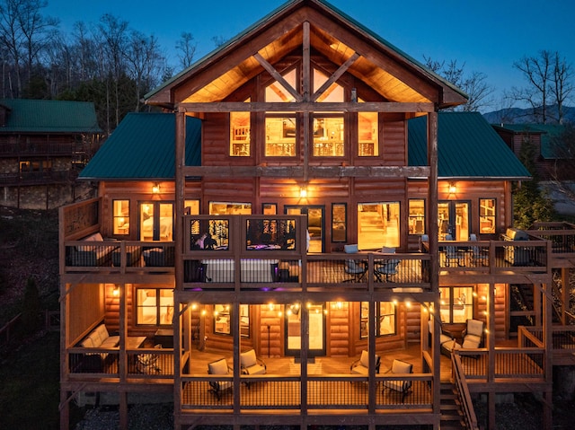 rear view of house with faux log siding, metal roof, a balcony, and a wooden deck