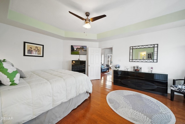 bedroom with ceiling fan, a raised ceiling, and wood finished floors