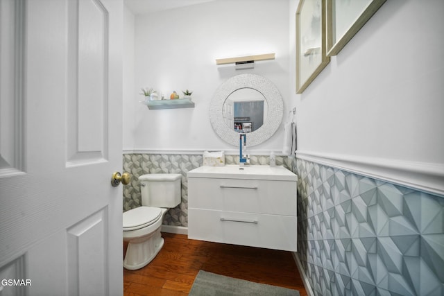 half bath featuring a wainscoted wall, tile walls, toilet, vanity, and wood finished floors