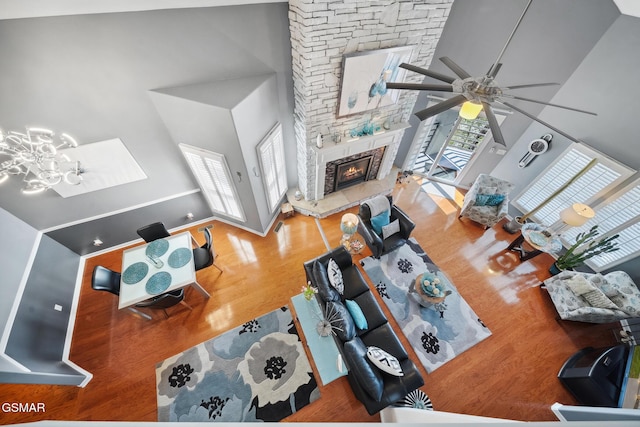 living room featuring a stone fireplace, wood finished floors, a towering ceiling, and a ceiling fan