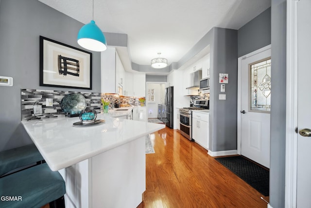 kitchen with white cabinets, appliances with stainless steel finishes, a peninsula, light countertops, and a kitchen bar