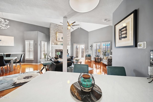 dining space featuring a ceiling fan, wood finished floors, a textured ceiling, a stone fireplace, and high vaulted ceiling