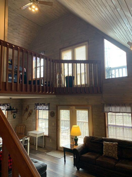 living room featuring wood walls, vaulted ceiling, ceiling fan, wood-type flooring, and wood ceiling