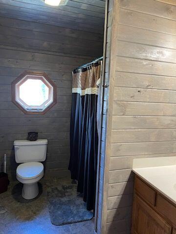 bathroom with a shower with curtain, vanity, toilet, and wood walls