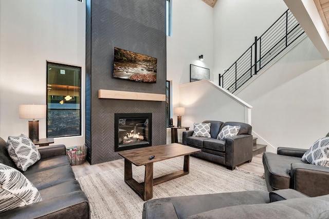 living area featuring a high ceiling, wood finished floors, a large fireplace, and stairs