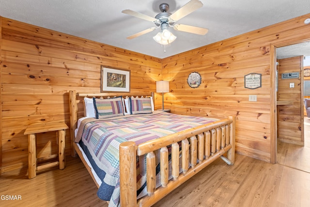 bedroom with ceiling fan, light hardwood / wood-style floors, a textured ceiling, and wood walls