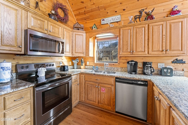 kitchen featuring stainless steel appliances, vaulted ceiling, light stone countertops, and sink