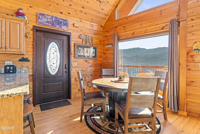 dining room featuring vaulted ceiling, a mountain view, light hardwood / wood-style floors, and wood walls