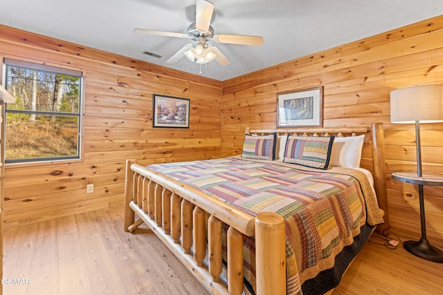 bedroom with wooden walls, ceiling fan, and light wood-type flooring