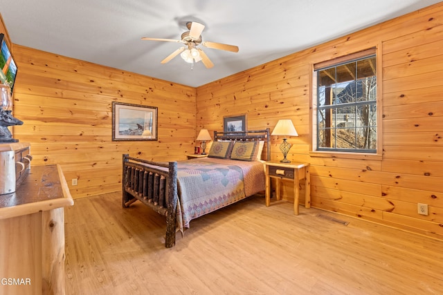 bedroom with wooden walls, ceiling fan, and light wood-type flooring