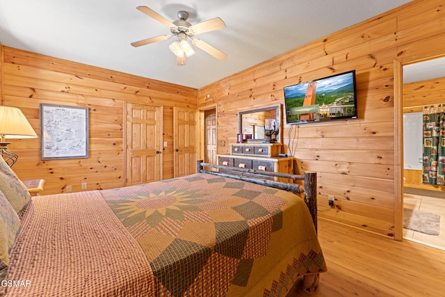 bedroom with ceiling fan, wooden walls, and light wood-type flooring