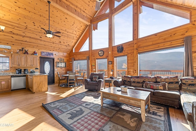 living room with wood walls, high vaulted ceiling, a mountain view, ceiling fan, and light hardwood / wood-style floors