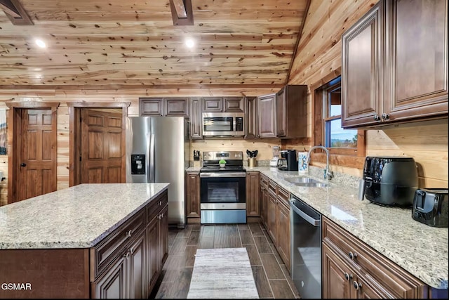 kitchen with wood tiled floor, vaulted ceiling, light stone counters, appliances with stainless steel finishes, and a sink