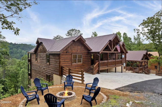 rear view of property featuring a patio, a wooden deck, metal roof, and an outdoor fire pit