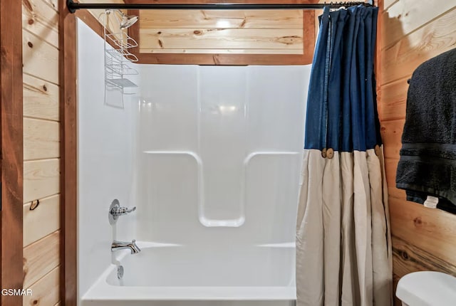 bathroom with wooden walls, shower / tub combo, and toilet