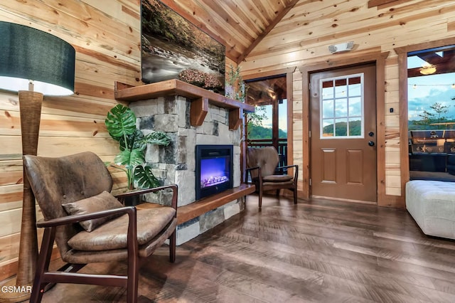 living area with wooden walls, wood ceiling, lofted ceiling, a stone fireplace, and wood finished floors