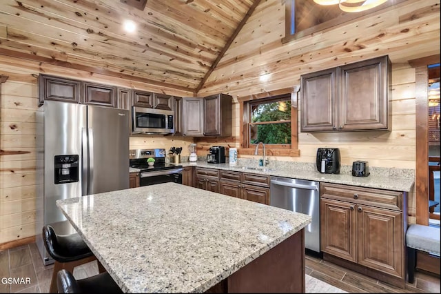 kitchen with wooden walls, lofted ceiling, appliances with stainless steel finishes, a kitchen breakfast bar, and wooden ceiling