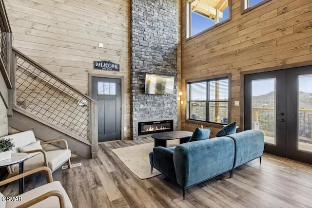 living room with a towering ceiling, french doors, a stone fireplace, wood finished floors, and wood walls
