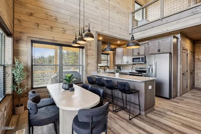 kitchen featuring stainless steel appliances, wooden walls, a towering ceiling, light wood finished floors, and a peninsula
