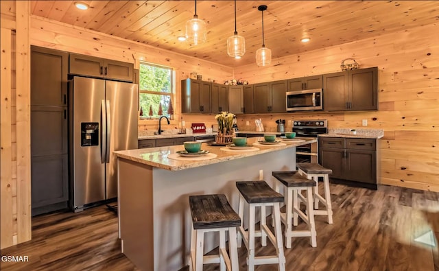 kitchen with appliances with stainless steel finishes, pendant lighting, sink, dark hardwood / wood-style flooring, and a center island