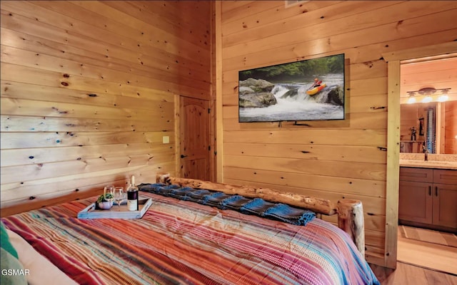 bedroom featuring connected bathroom, sink, light hardwood / wood-style flooring, and wood walls