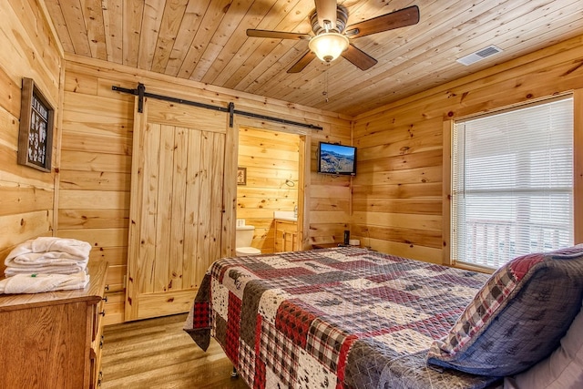 bedroom with ceiling fan, a barn door, wooden ceiling, and ensuite bath