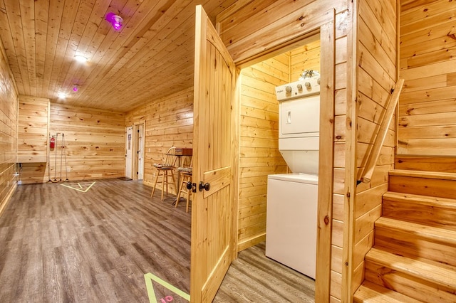 clothes washing area featuring hardwood / wood-style floors, stacked washing maching and dryer, wood walls, and wood ceiling