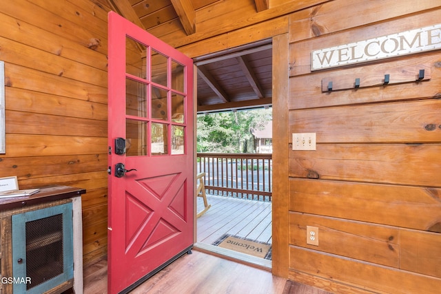 doorway to outside featuring wood ceiling, wooden walls, light hardwood / wood-style floors, and vaulted ceiling with beams